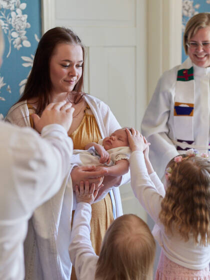En präst och en grupp andra människor välsignar ett barn i dopkolt.