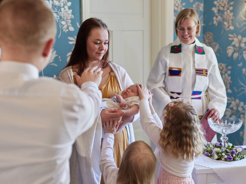 En präst och en grupp andra människor välsignar ett barn i dopkolt.