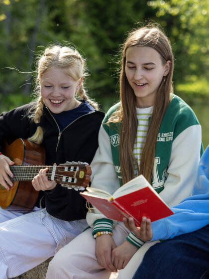 Three girls are singing. One has a guitar and another a song book.