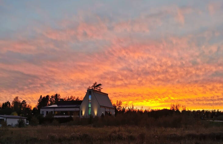 Söderkullan kirkko kuvattuna auringonlaskun aikaan. Kirkon takana oranssi auringonlasku.